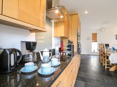 A kitchen counter with a kettle coffee maker teapot cups and saucers next to a dining area with wooden chairs and a table at Osprey House Portland