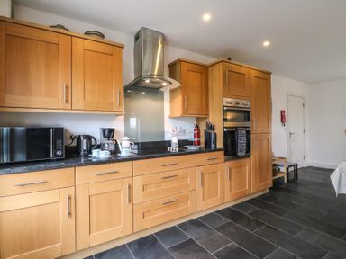 A kitchen with wooden cabinets black countertop microwave coffee maker kettle oven and black tiled floor at Osprey House Portland