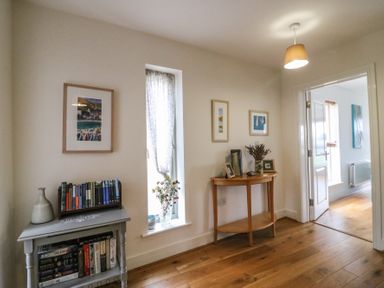 A hallway with wooden floor a small table with books a window with sheer curtain and flowers and a wooden console table with decorations at Osprey House Portland