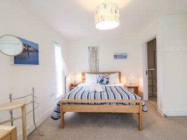 A bedroom with a wooden bed with striped bedding two bedside tables with lamps and an open door to a bathroom at Osprey House Portland