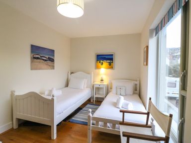 A bedroom with two single beds a bedside table with a lamp a wooden chair and paintings on the walls at Osprey House Portland in Portland
