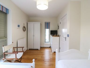 A bedroom with white bed frames wooden floor wardrobe dresser chair and a window at Osprey House Portland