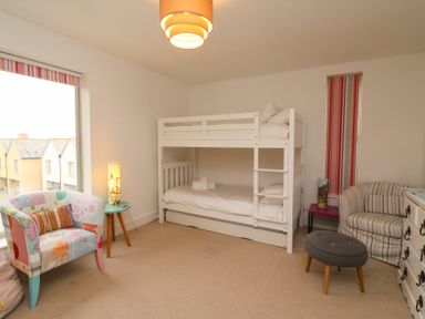 A bedroom with a white bunk bed two armchairs a small round table with a lamp and a window with striped blinds at Osprey House Portland