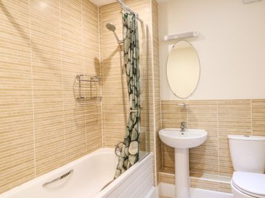A bathroom with a bathtub shower combination a round mirror a pedestal sink and a toilet at Osprey House Portland