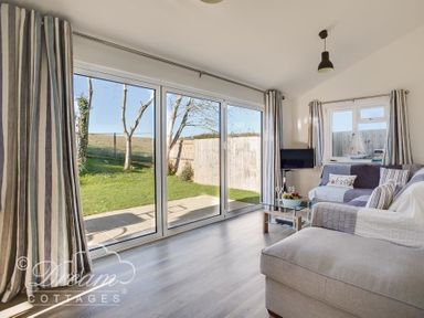 A living room with a sofa a glass coffee table a small TV and large sliding glass doors overlooking a garden at Outlook Lodge in Bowleaze