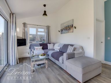 A living room with a sectional sofa a glass coffee table and a TV mounted on the wall at Outlook Lodge in Bowleaze