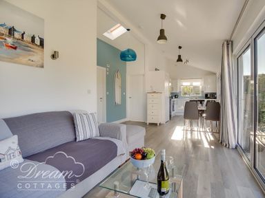 An open living room and kitchen with a sofa glass coffee table dining table and large sliding glass doors at Outlook Lodge in Bowleaze