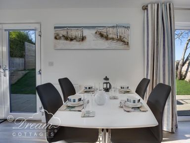 A dining table set for four with black chairs in a room with glass doors and curtains at Outlook Lodge in Bowleaze