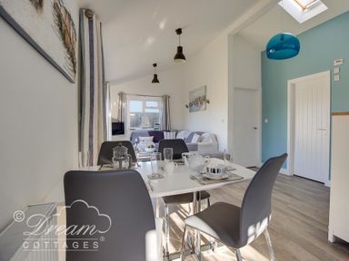A dining table with chairs and tableware in a room with a sofa and blue accent wall at Outlook Lodge in Bowleaze