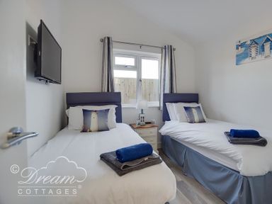 A bedroom with two single beds with lighthouse pillows and folded towels between a window at Outlook Lodge in Bowleaze