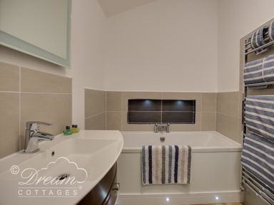 A bathroom with a sink, a bathtub with a striped towel, and a towel rack with striped towels at Outlook Lodge in Bowleaze