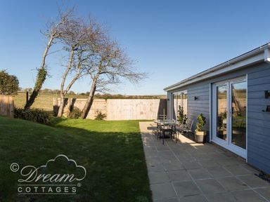 A backyard with a tiled patio table and chairs a blue house wooden fence and leafless trees at Outlook Lodge in Bowleaze