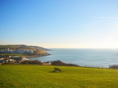 A grassy hill with a bench overlooking a coastal town and the ocean at Outlook Lodge in Bowleaze