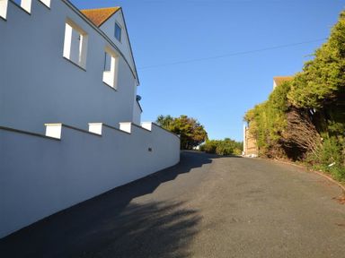 A paved driveway with a white wall on the left and dense shrubbery on the right at Outlook Lodge in Bowleaze