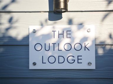 A wall-mounted sign with the text The Outlook Lodge on a grey wooden exterior