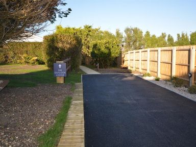 A paved driveway with a wooden fence on the right and a sign pointing to The Outlook Lodge at Bowleaze