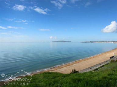 A sandy beach with calm water and a grassy hill at Outlook Lodge in Bowleaze