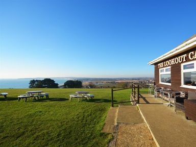 An outdoor seating area with picnic tables on grass near a building with a view of the coast at Outlook Lodge in Bowleaze