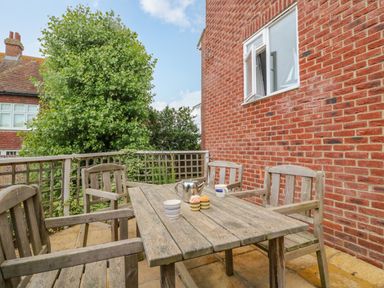 An outdoor patio with a wooden table and four wooden chairs a teapot and cups on the table next to a red brick house with a window at Ocean Watch 1 Greenhill