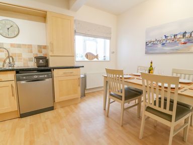 A kitchen and dining area with a dishwasher wooden cabinets dining table and chairs and a painting on the wall at Ocean Watch 1 in Greenhill