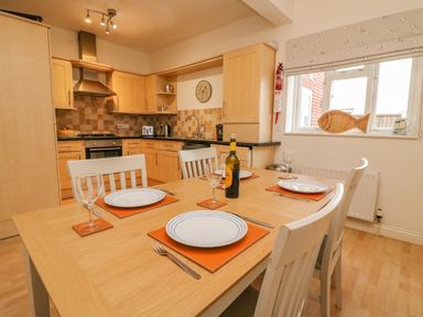 A kitchen with wooden cabinets a dining table set with plates glasses and cutlery at Ocean Watch 1 in Greenhill
