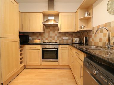 A kitchen with wooden cabinets black countertops stainless steel oven and sink at Ocean Watch 1 in Greenhill