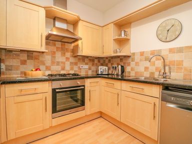 A kitchen with wooden cabinets a gas stove an oven a toaster a kettle a sink a dishwasher and a wall clock at Ocean Watch 1 in Greenhill