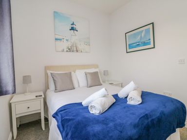 A bedroom with a double bed blue blanket rolled white towels bedside tables and wall art at Ocean Watch 1 in Greenhill
