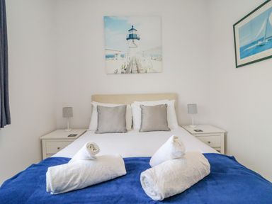 A bedroom with a bed with pillows and rolled towels on a blue blanket and nightstands with lamps at Ocean Watch 1 in Greenhill