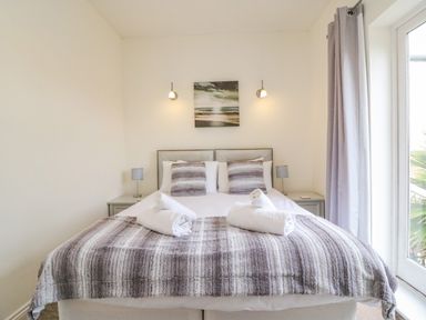 A bedroom with a double bed two bedside tables with lamps wall lights and a window with curtains at Ocean Watch 1 in Greenhill