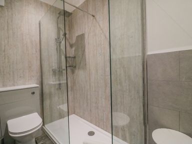 A bathroom with a toilet and a glass-enclosed shower with wood-textured walls at Ocean Watch 1 in Greenhill