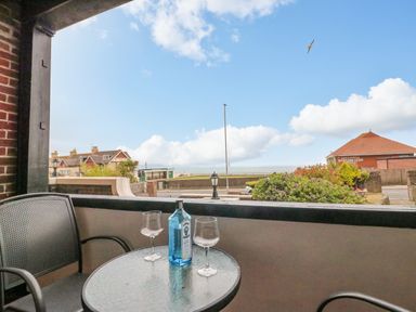 A balcony with a round glass table holding a blue bottle and two wine glasses with chairs overlooking houses and a greenhill bowling club in Greenhill