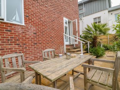 A patio with a wooden table and chairs outside a brick house with an open door and plants nearby at Ocean Watch 1 in Greenhill