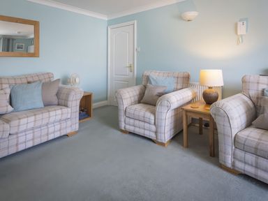A living room with three plaid armchairs a wooden side table with a lamp a wall mirror and a door at Bakers Dozen 13 Dartmouth House in Dartmouth