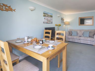 A dining table set with plates cups and croissants in a living room with a sofa and a television at Bakers Dozen 13 Dartmouth House in Dartmouth