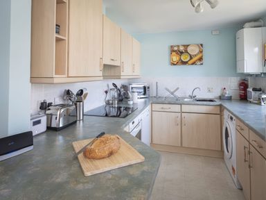 A kitchen with wooden cabinets a loaf of bread on a cutting board and various appliances at Bakers Dozen 13 Dartmouth House in Dartmouth