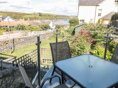 An outdoor seating area with a glass table and chairs overlooking a garden with stone walls and houses in the background at 14a Courtenay Street Salcombe