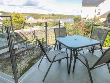 An outdoor patio with a glass table and four chairs and a view of stone walls greenery and distant water at 14a Courtenay Street in Salcombe