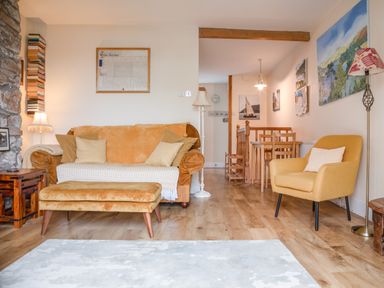 A living room with a sofa, armchair, ottoman, floor lamps, wooden side table, and dining table with chairs at 14a Courtenay Street in Salcombe