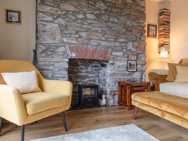 A living room with a stone fireplace yellow armchair and wooden side tables at 14a Courtenay Street in Salcombe