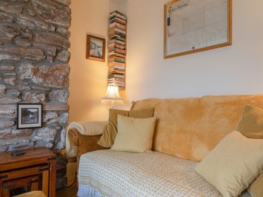 A living room with a yellow couch pillows a stone wall a wooden table a lamp and books at 14a Courtenay Street in Salcombe