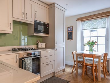 A kitchen with white cabinets a gas stove microwave and a dining table with flowers at 14a Courtenay Street in Salcombe