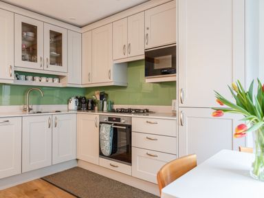 A kitchen with white cabinets a built-in oven stovetop coffee machine kettle and a vase of tulips on a table at 14a Courtenay Street in Salcombe