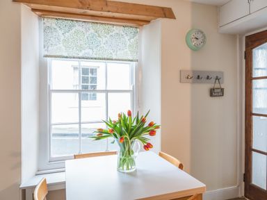 A dining area with a white table and tulips in a glass vase near a window with a floral roller blind at 14a Courtenay Street in Salcombe