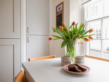 A kitchen table with a vase of tulips two mugs and a plate of cookies at 14a Courtenay Street in Salcombe