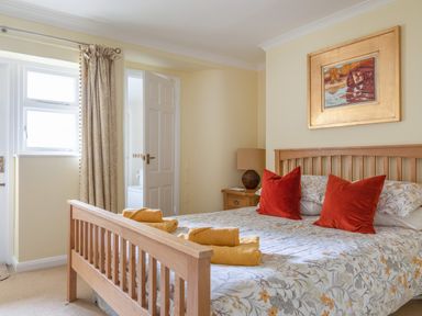 A bedroom with a wooden bed frame floral bedding red pillows yellow towels and a nightstand with a lamp at 14a Courtenay Street in Salcombe