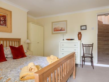 A bedroom with a wooden bed, two rolled towels, a white dresser, a wooden chair, and carpeted stairs at 14a Courtenay Street in Salcombe