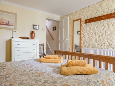 A bedroom with a bed with towels on it a white chest of drawers a chair a wall mirror and a partially open door at 14a Courtenay Street in Salcombe
