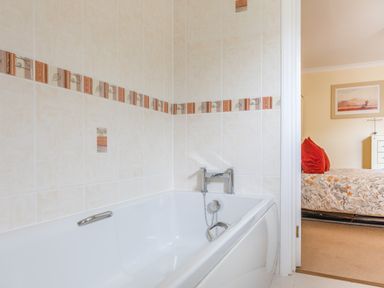 A bathroom with a white bathtub and patterned beige tiles next to a bedroom with a bed and orange pillows at 14a Courtenay Street in Salcombe