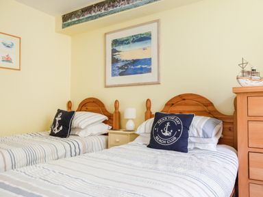 A bedroom with two wooden single beds striped bedding decorative pillows and framed beach artwork at 14a Courtenay Street in Salcombe